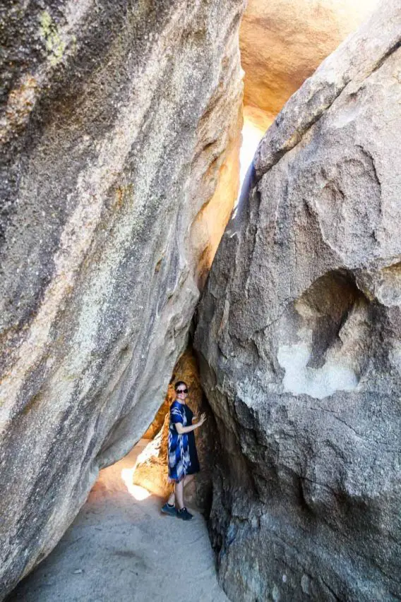 Woman standing in gap between large rocks where sunlight shines through