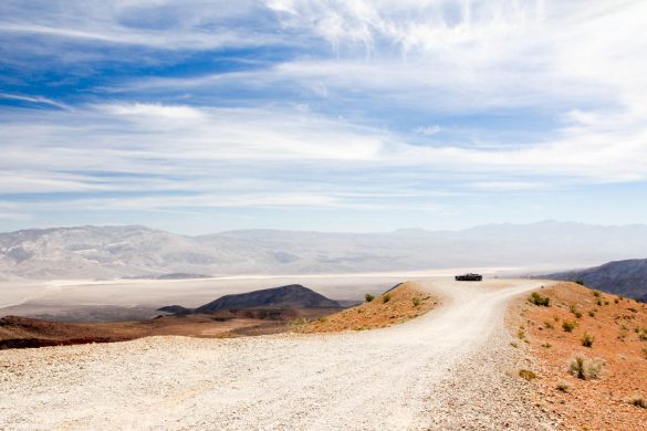 A black car parked on a dirt cul-de-sac overlooking a desert valley