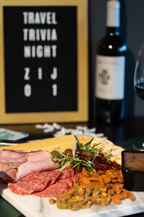 Photo of tabletop with charcuterie board, wine and travel trivia scoreboard