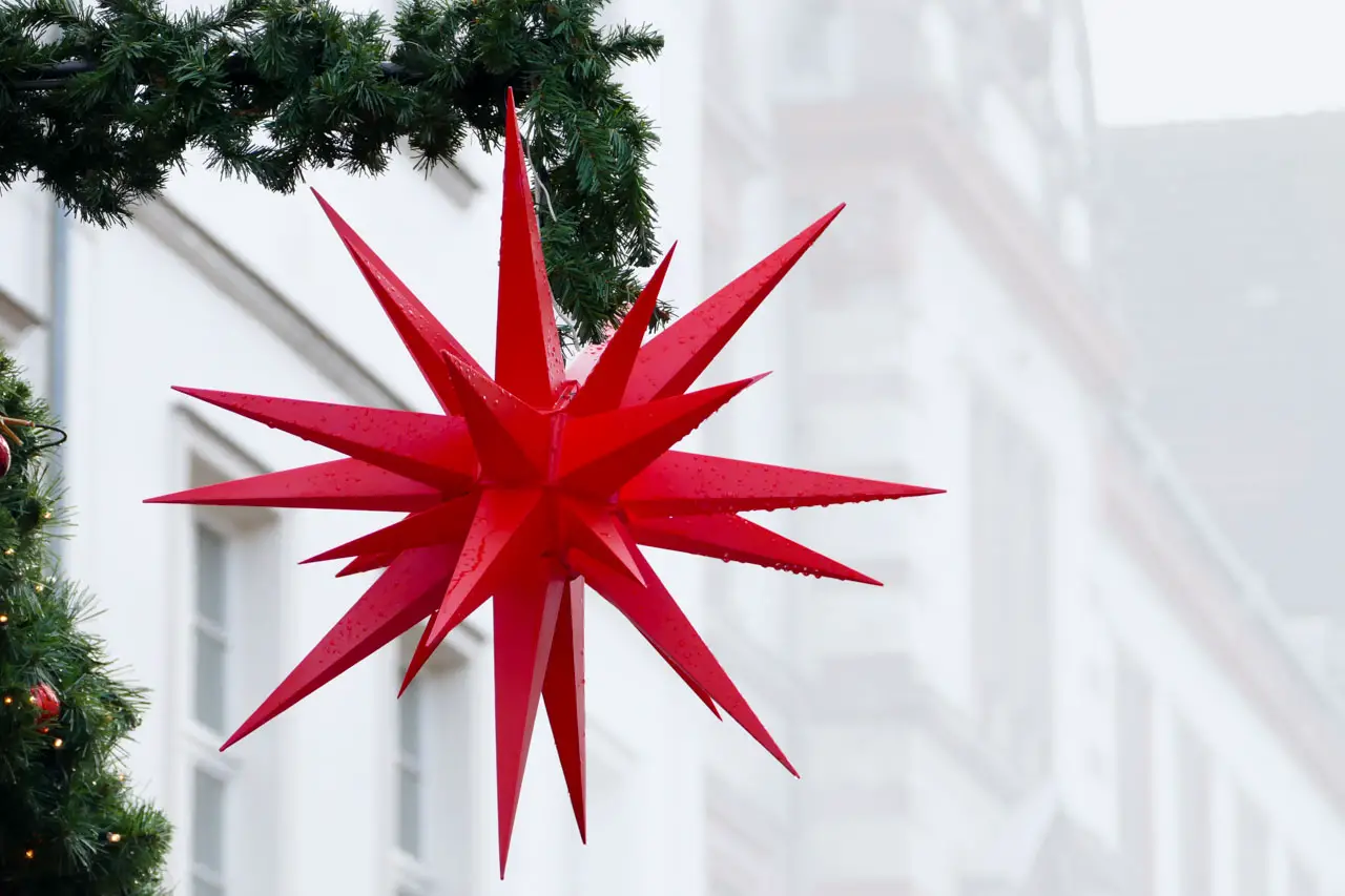 Red Moravian star hanging from evergreen garland in street.