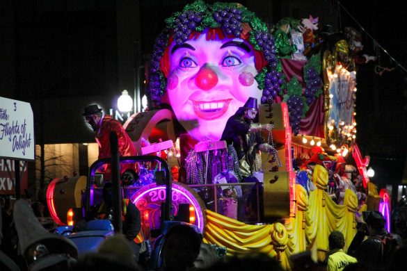 Parade float with giant clown face dressed as Bachhus with grape vines.