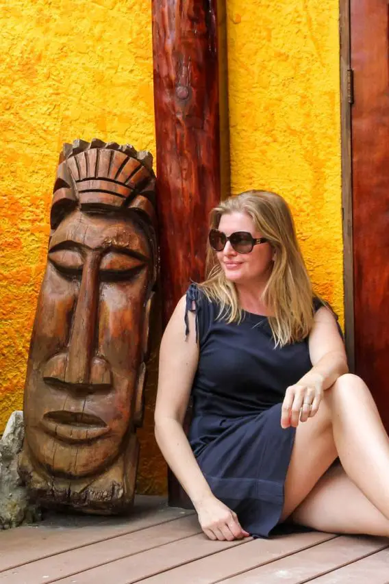 Madam ZoZo in Belize, sitting next to wooden carving of face