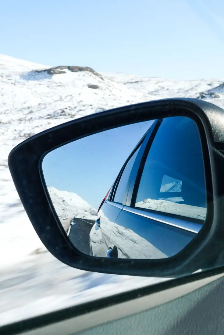 Rearview mirror showing raod through snow-covered highlands