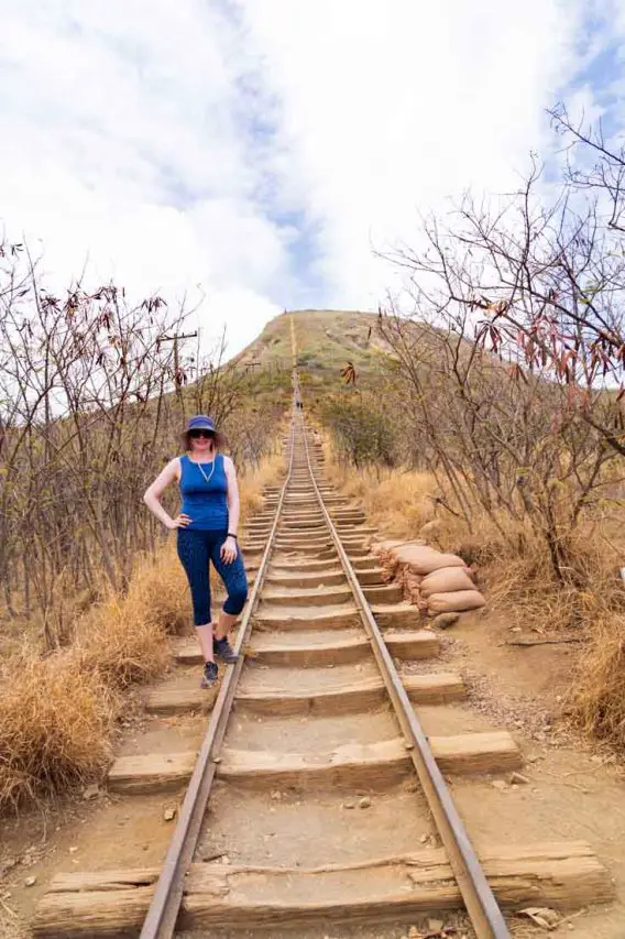 Woman in workout clothing standing beside railroad leading up a steep hillside