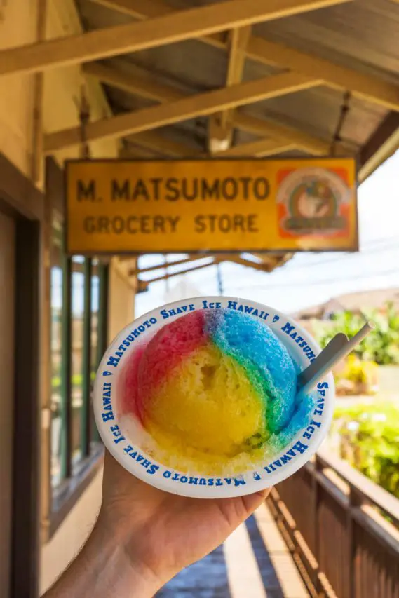 Bowl of shave ice in blue, yellow and red infront of M. Matsumoto Grocery Store sign