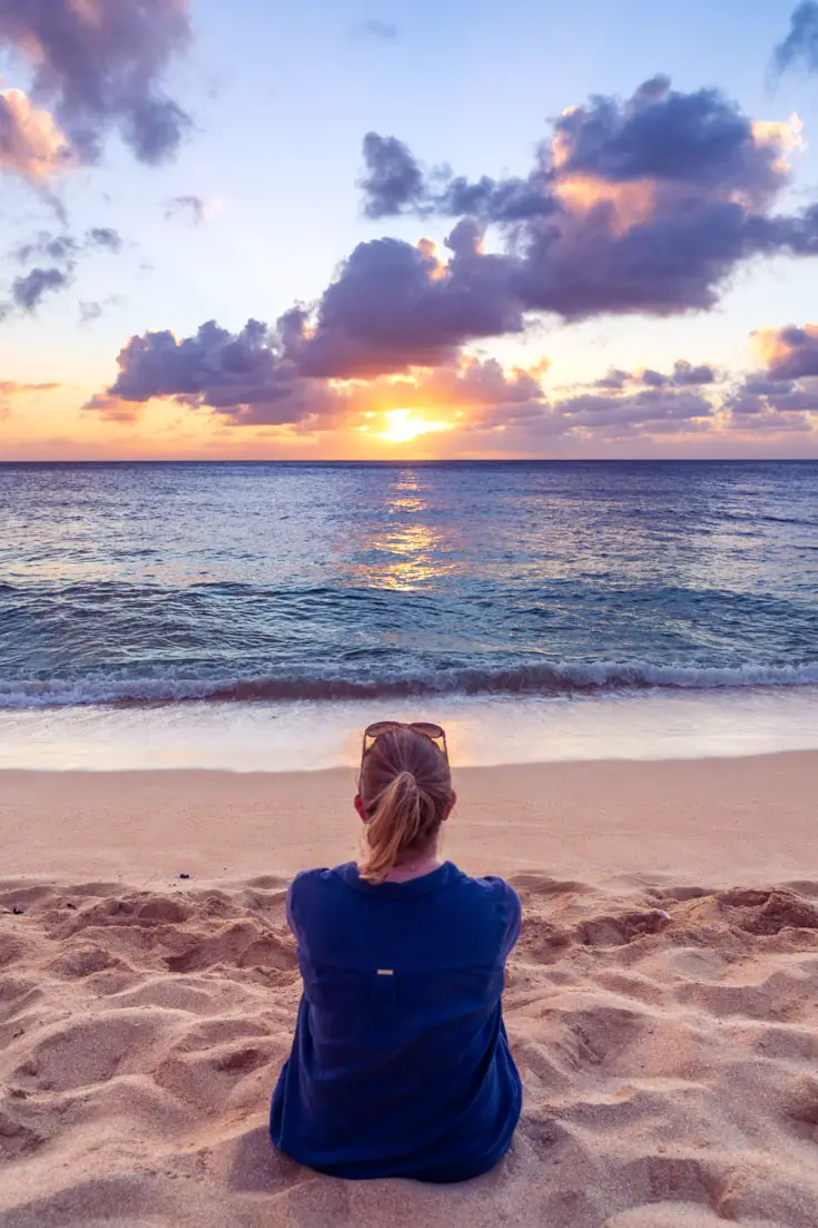 Woman sitting on beach looking out across water at beautiful sunset