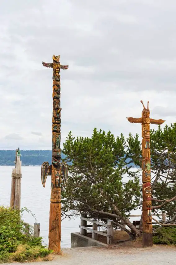 Two totem poles on the edge of the water with trees