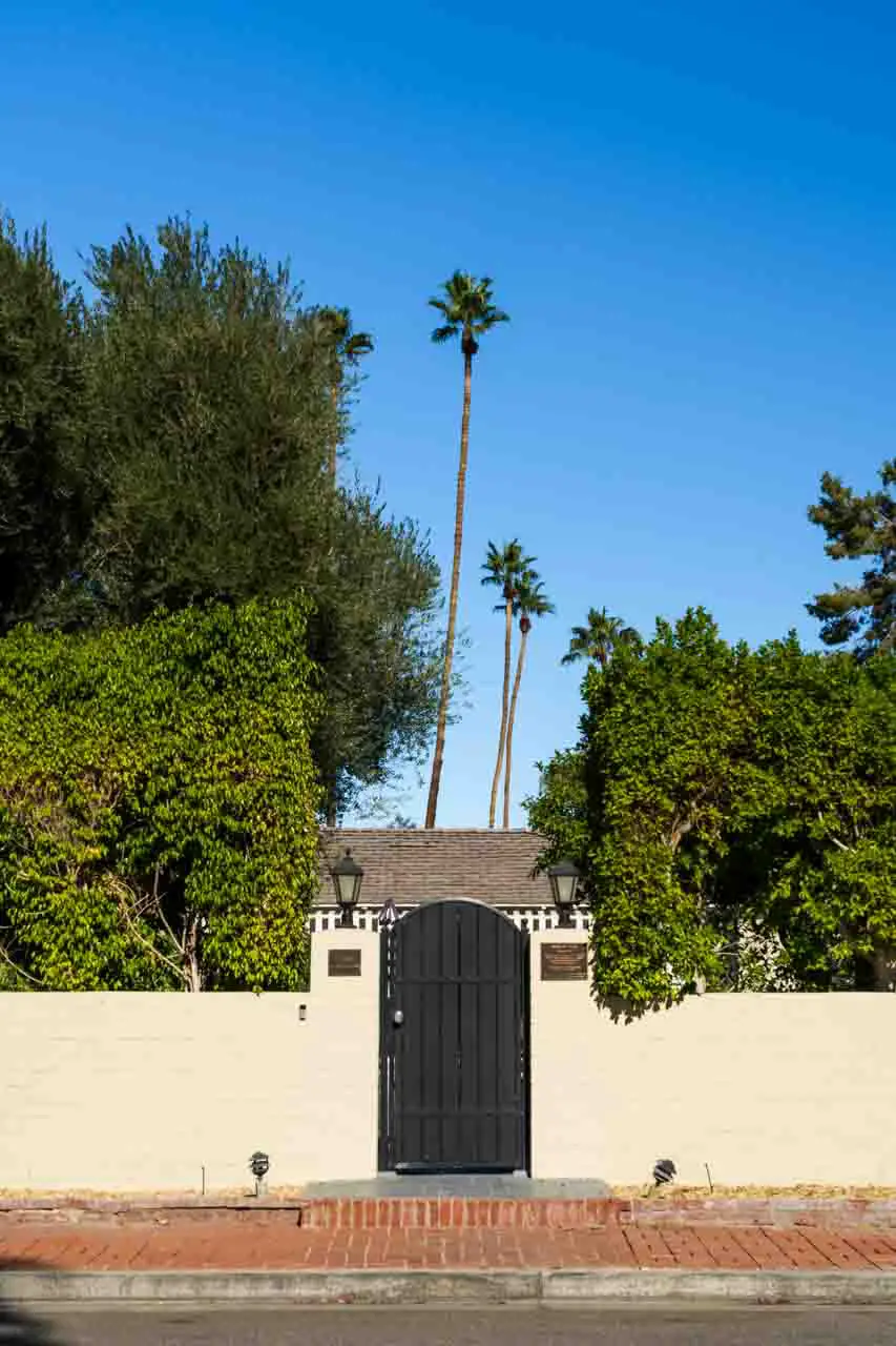 Black front gate in cream fence with hedging and palm trees