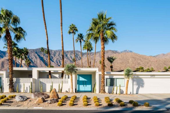 Mid-Century home in white with aquamarine front door, neat succulent garden and desert mountains behind.