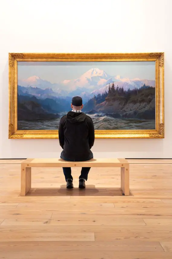 Man seated infront of large-scale, romantic landscape of Denali