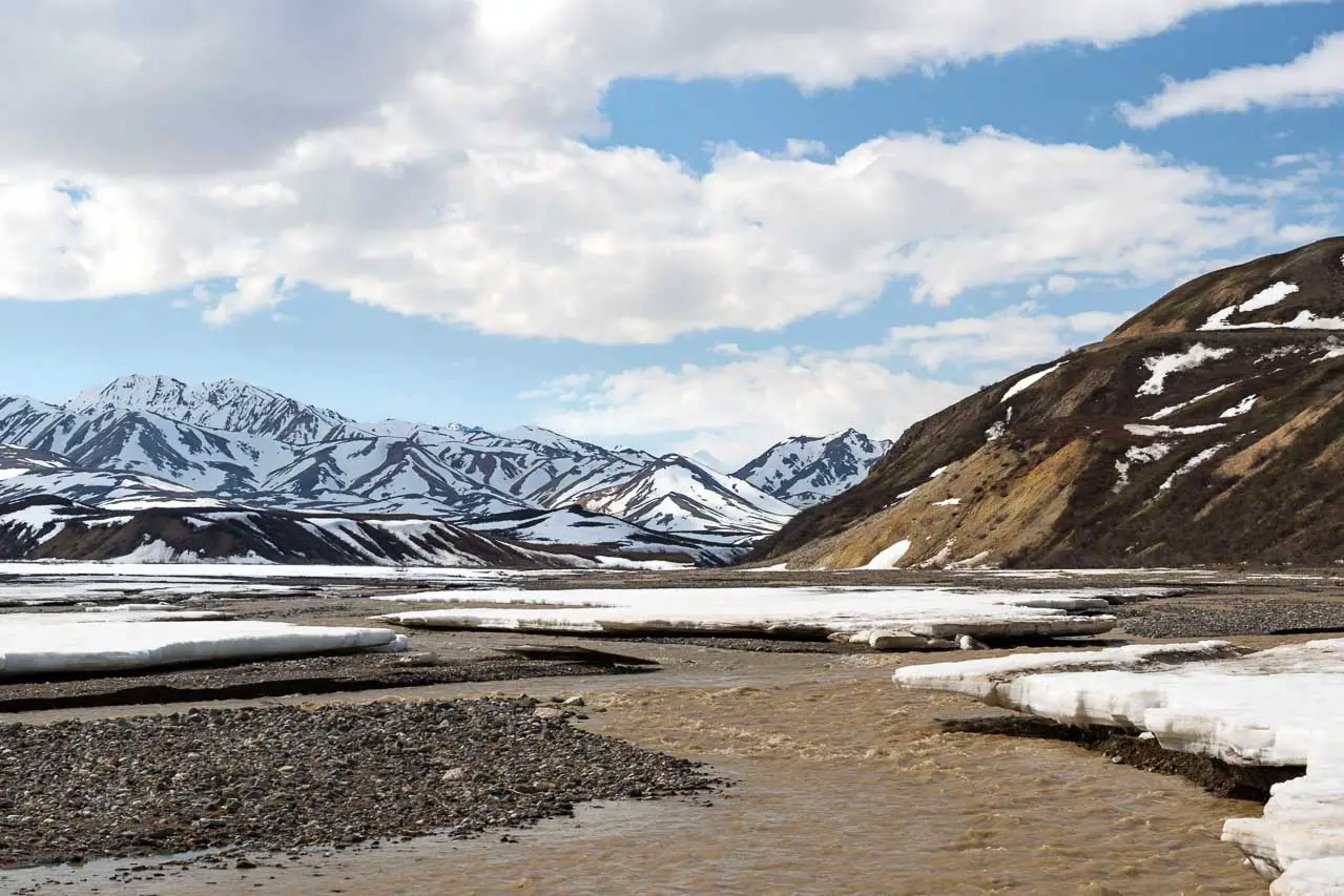 Ice melting on river bed with snowy mountains in background