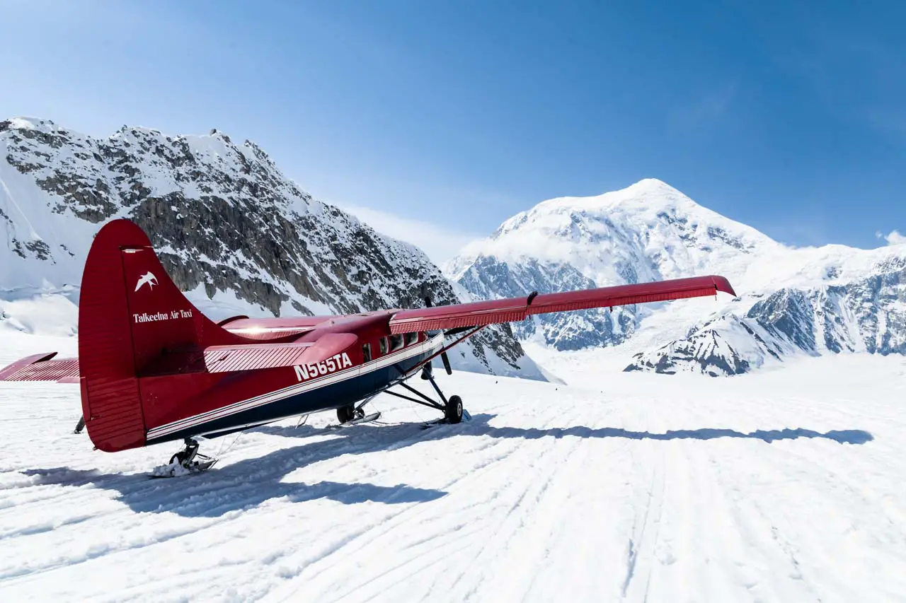 Small, red, ski plane on glacier surrounded by mountain peaks 