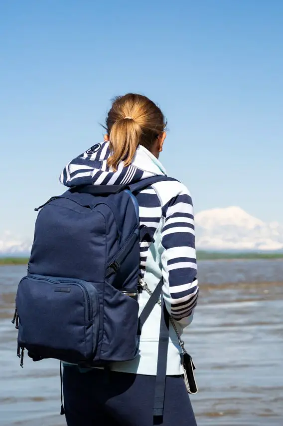 Woman with blue backpack looking out across river to snowy mountains