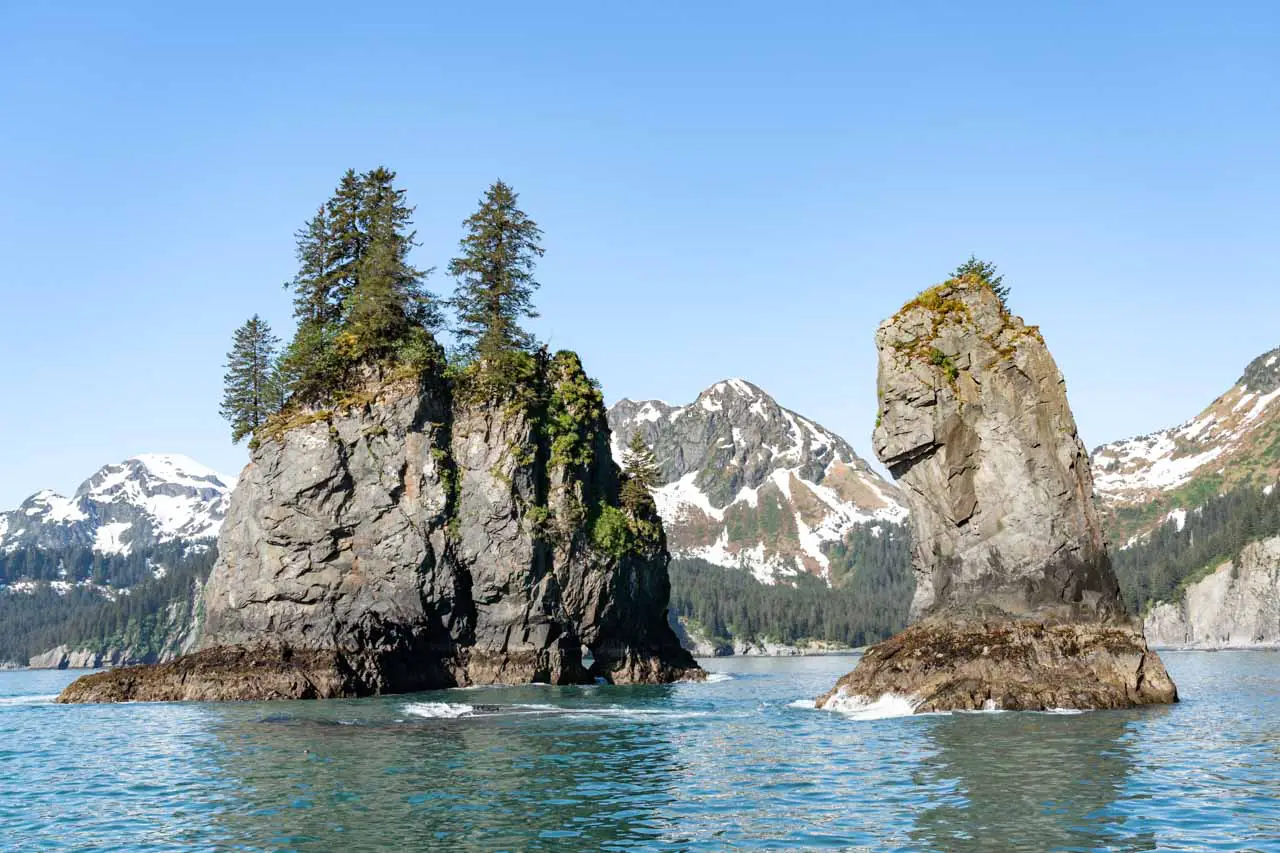 Small rock islands with evergreen trees and mountains in background.
