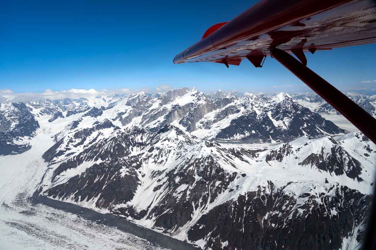 Red wing of plane framing photo of snow-covered mountains