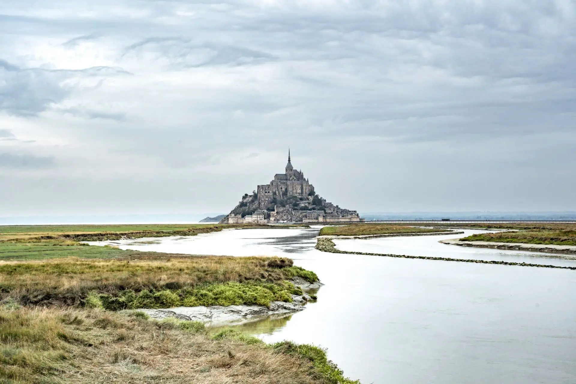 Mont St Michel on a grey, cloudy day with the Couesnon River in the foreground