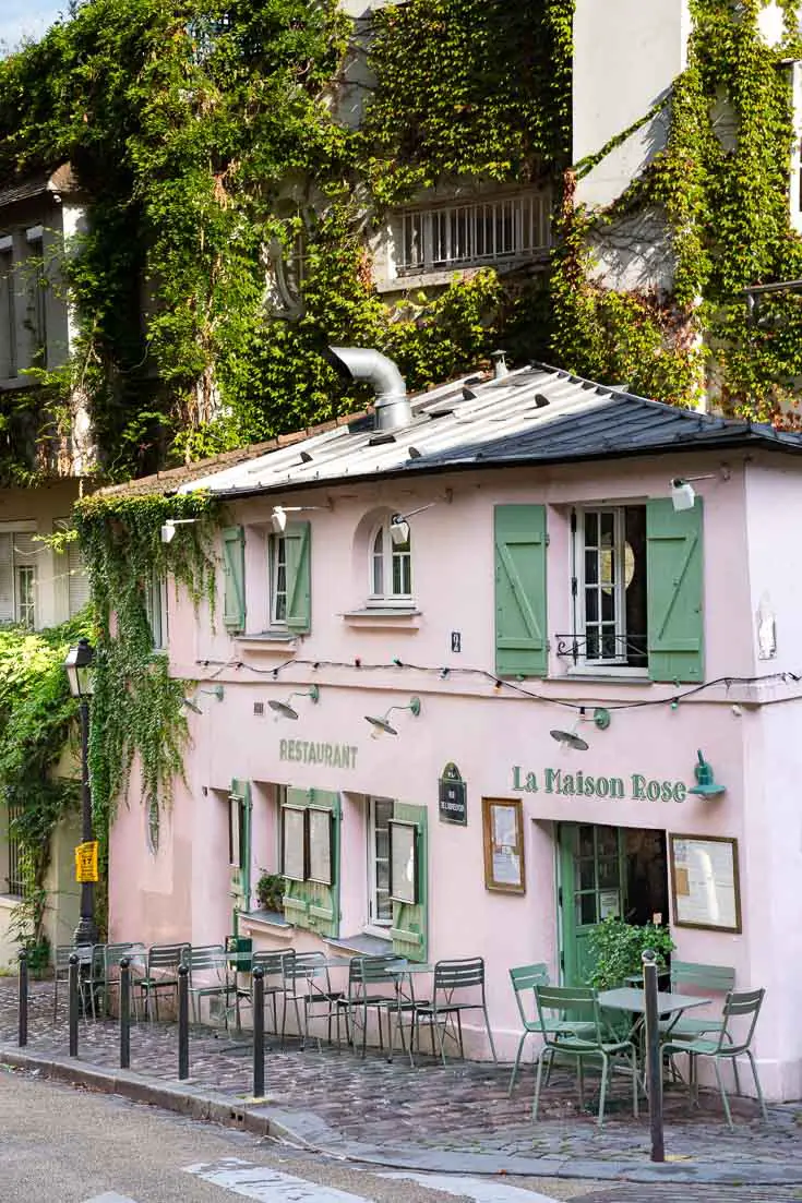 Pink restaurant with green shutters and tables out on the cobblestone footpath