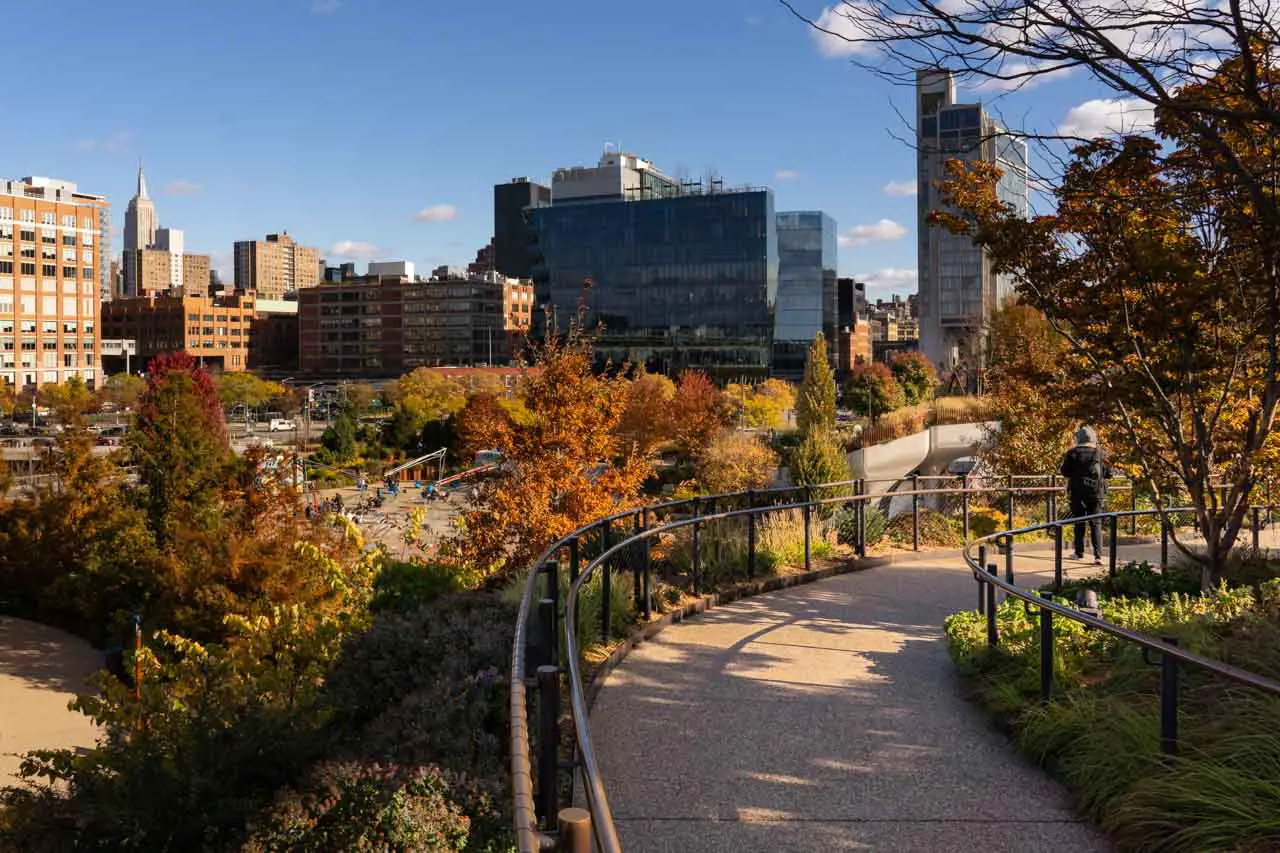 Autumn foliage on Little Island with walking path in foreground and Manhattan buildings in background
