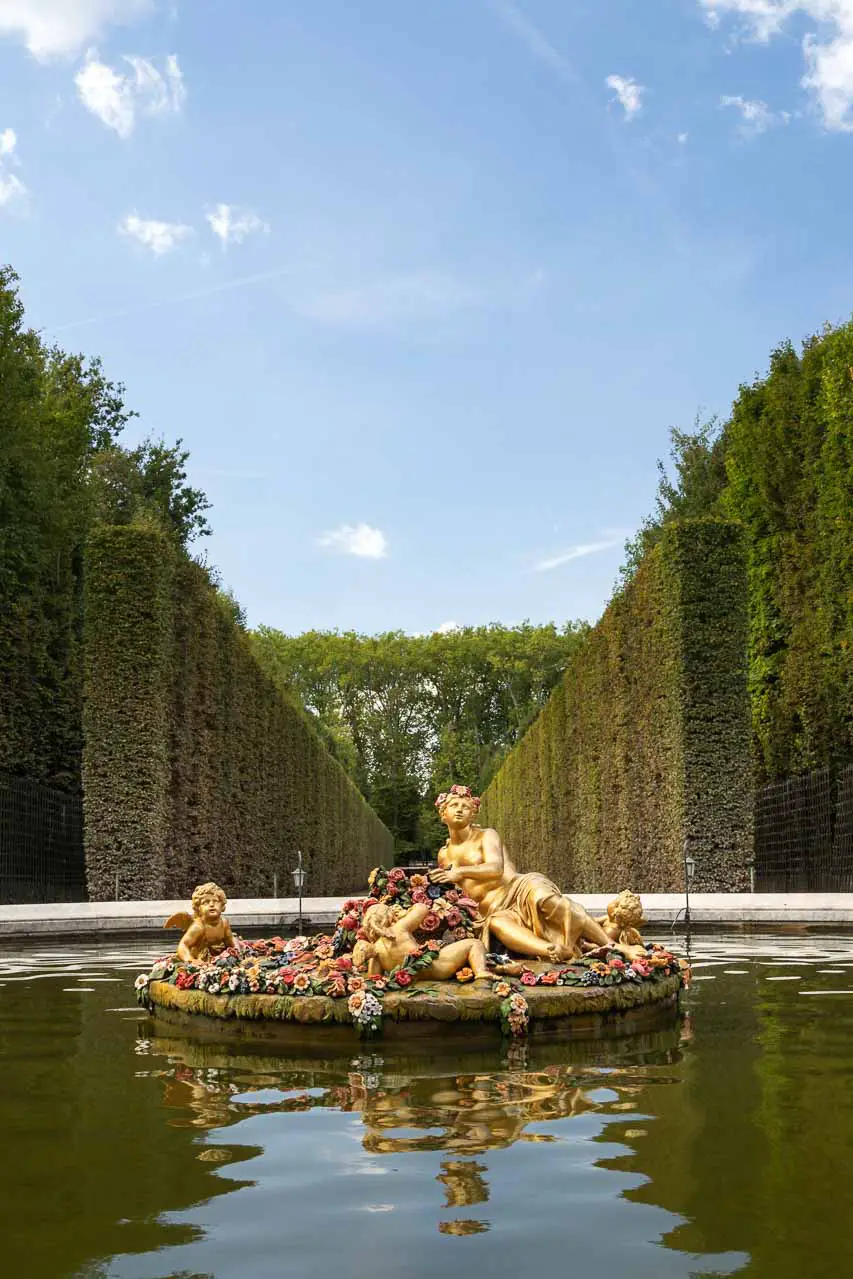 Gold fountain featuring Roman goddess Flora surrounded by flowers and framed by hedgerows