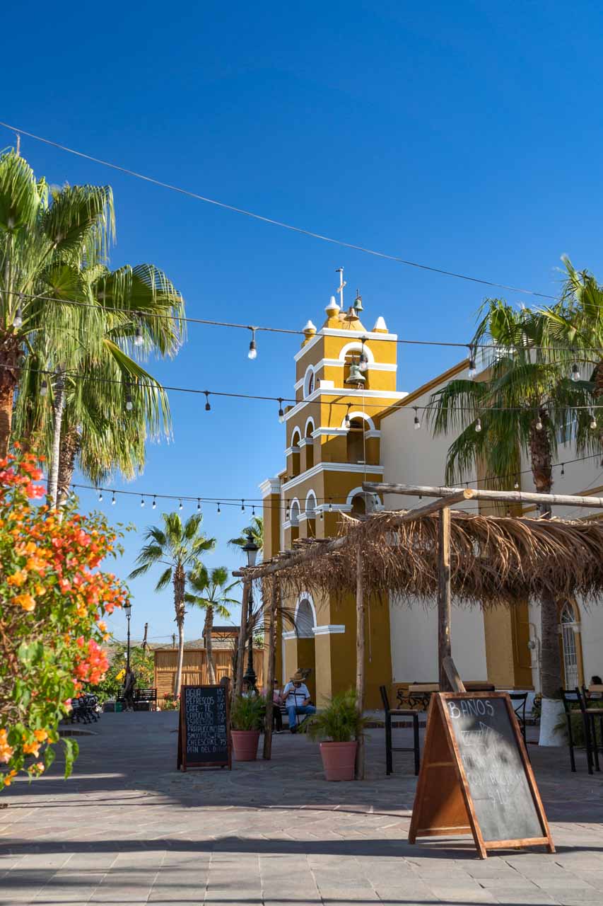 Yellow missionary building with palm trees and string lights in street