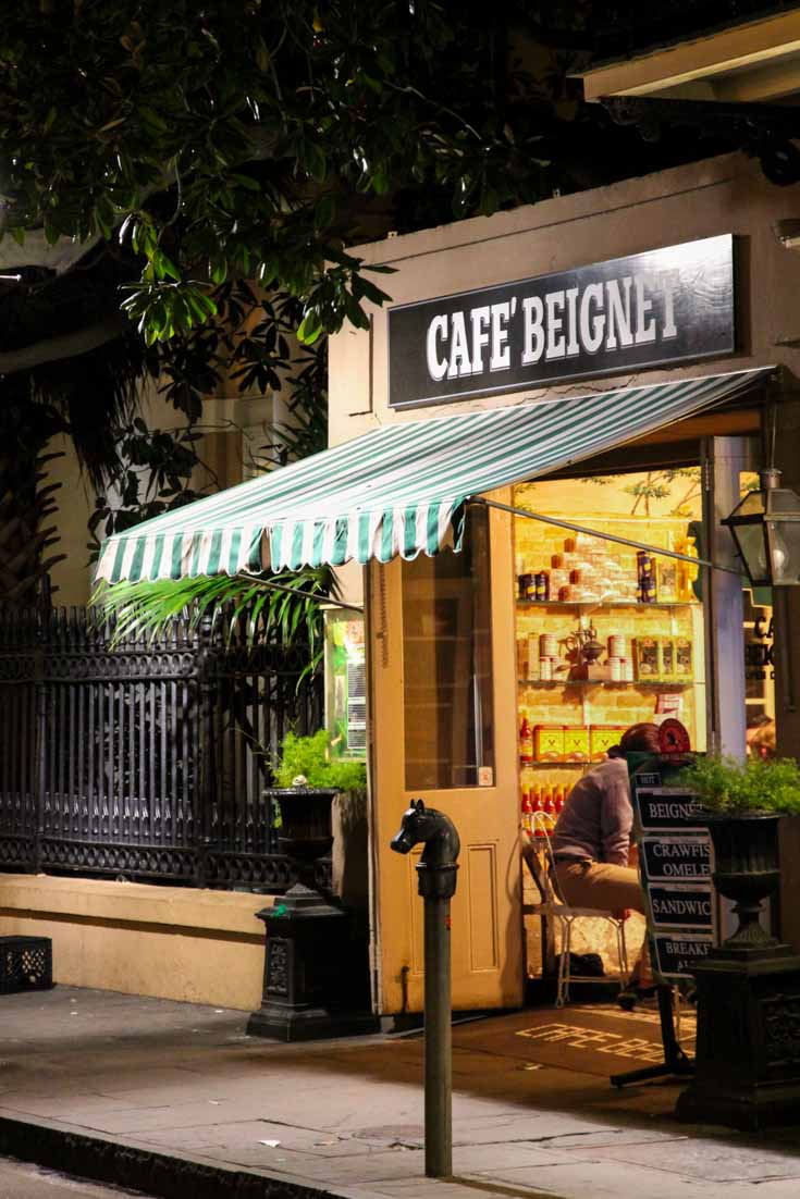 Street view of Cafe Beignet at night with golden lighting radiating from inside and a streetlamp-illuminated green and white awning.