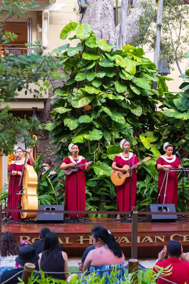 Four women performing traditional Hawai'ian music on stage backed by tropical plants
