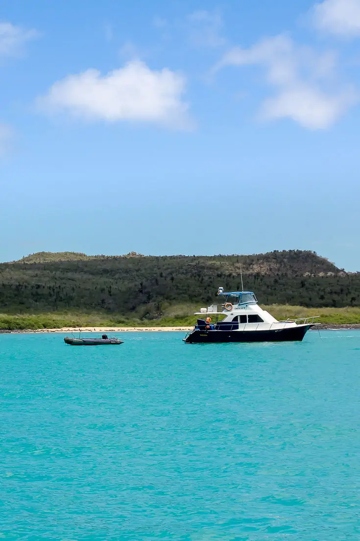 Motor boat with tender moored in aquamarine water off a low-lying island 