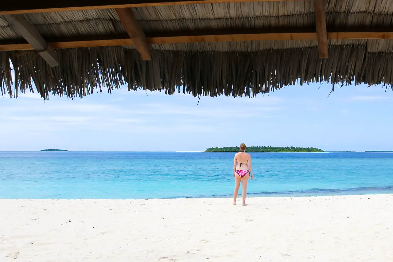 Woman in pink bikini looking out at crystal blue water and small, distant island