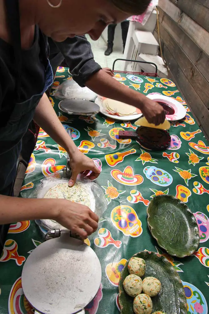 People pressing tortillas on table with green tablecloth