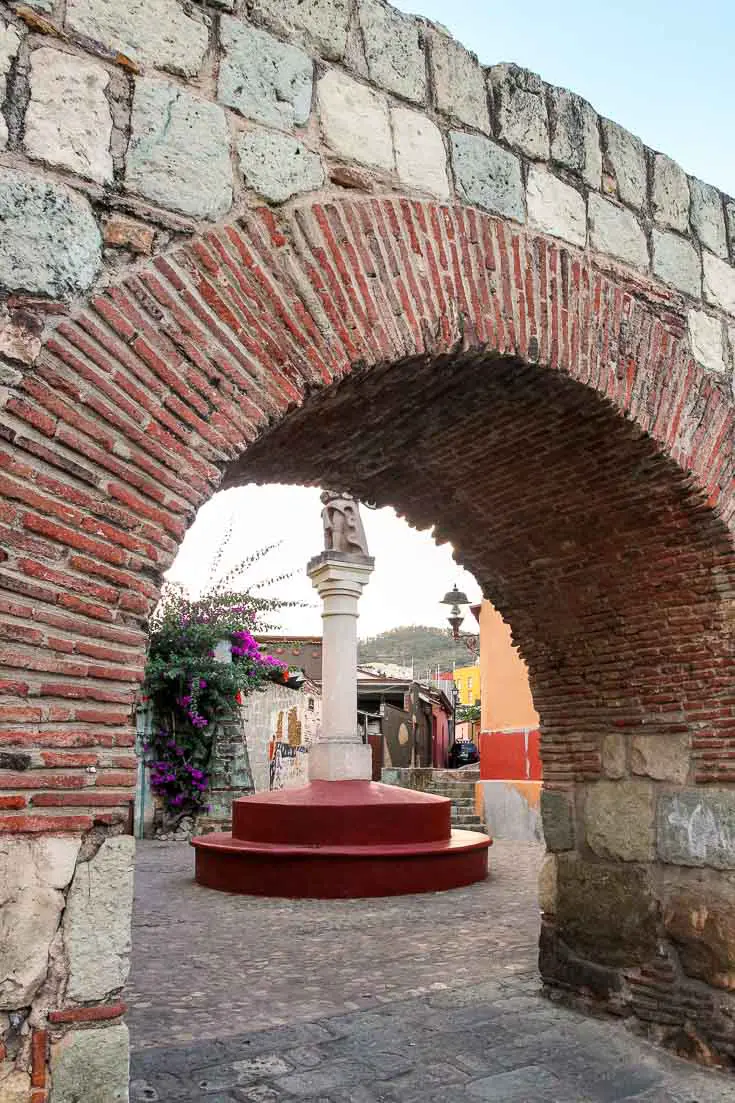View through arch of aquaduct to fountain and city street on the other side
