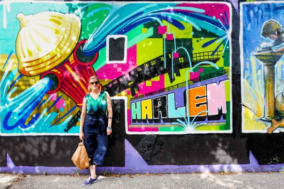 Woman in blue and green leaning against colourful mural with the word "Harlem"